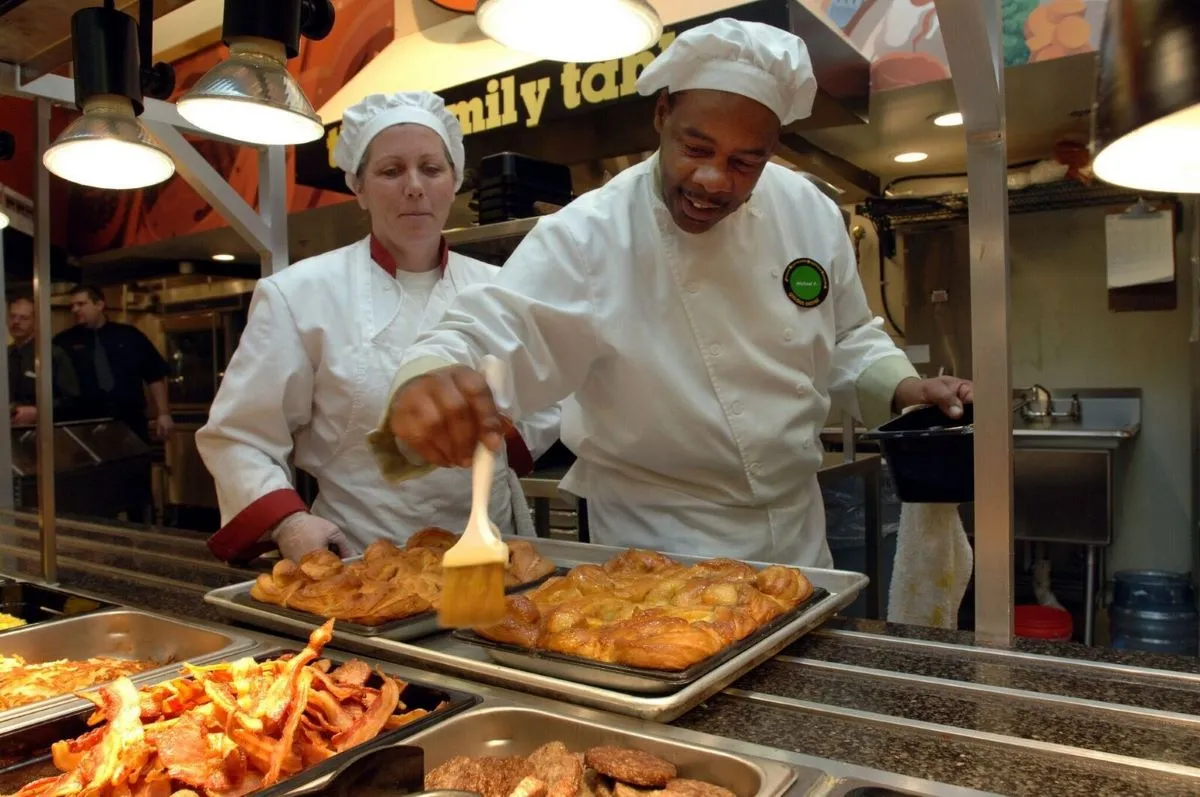 Two chefs at Golden Corral wearing white with one spreading butter with a brush on rolls