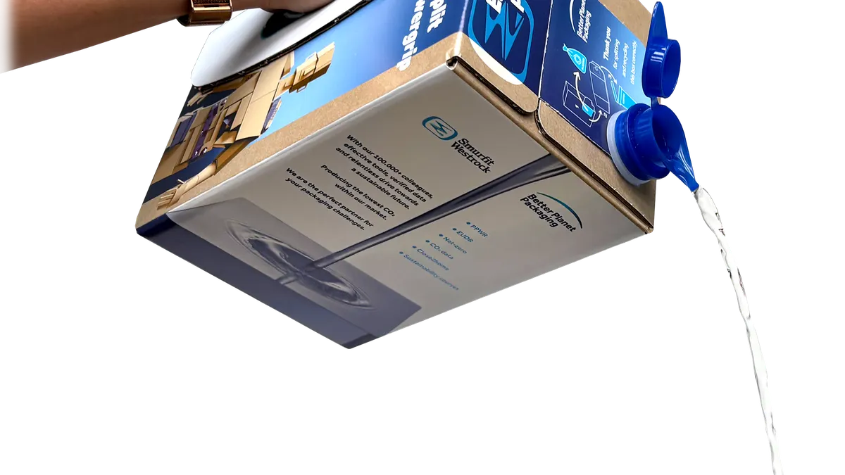 A person's hand holds a cardboard box via an integrated handle and pours fluid from a spout on the box.