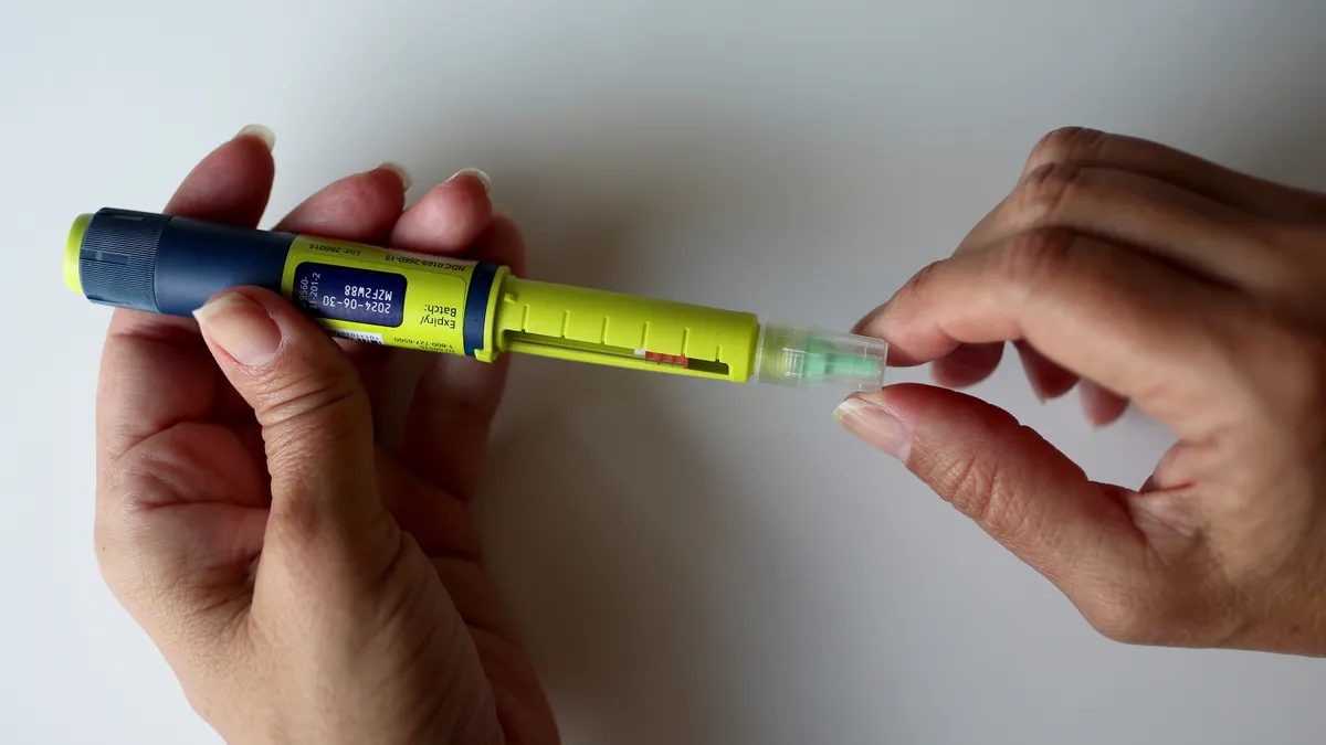 A person holds a yellow and blue pen, showing the expiration date.