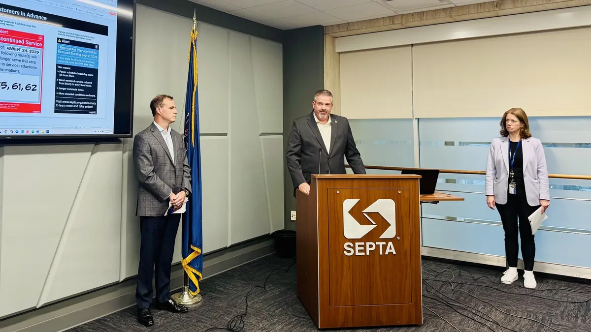 A in a suit standing at podium lettered "SEPTA" with a woman on his left and another man to his right.