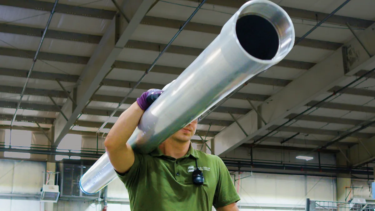 Construction worker carrying large steel pipe