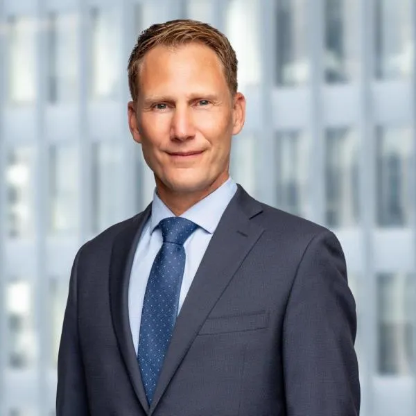 A headshot of a man wearing a grey suit and blue tie.
