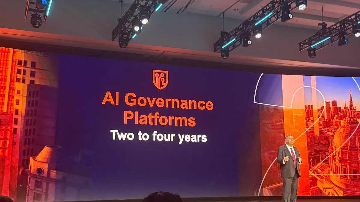 an analyst in business attire speaks on stage, with a screen in the background showing the text AI Governance Platforms.