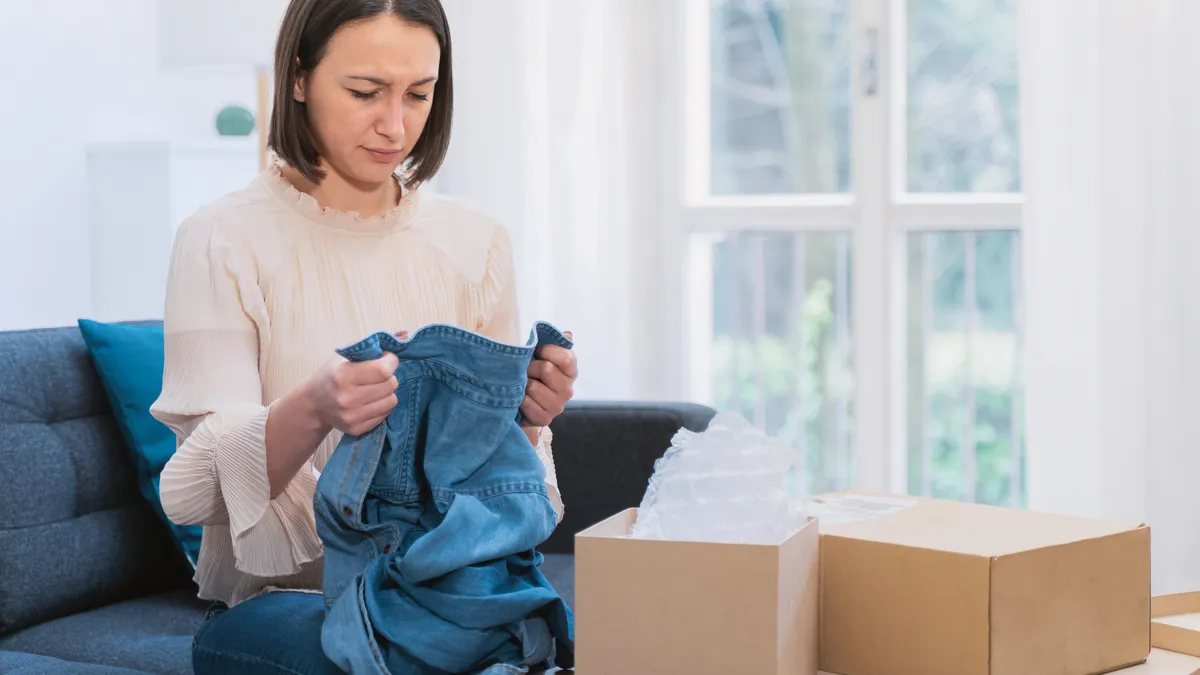 Dissatisfied young woman taking clothes out of box