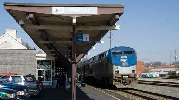 An Amtrak train stopped by a train station with parked cars.