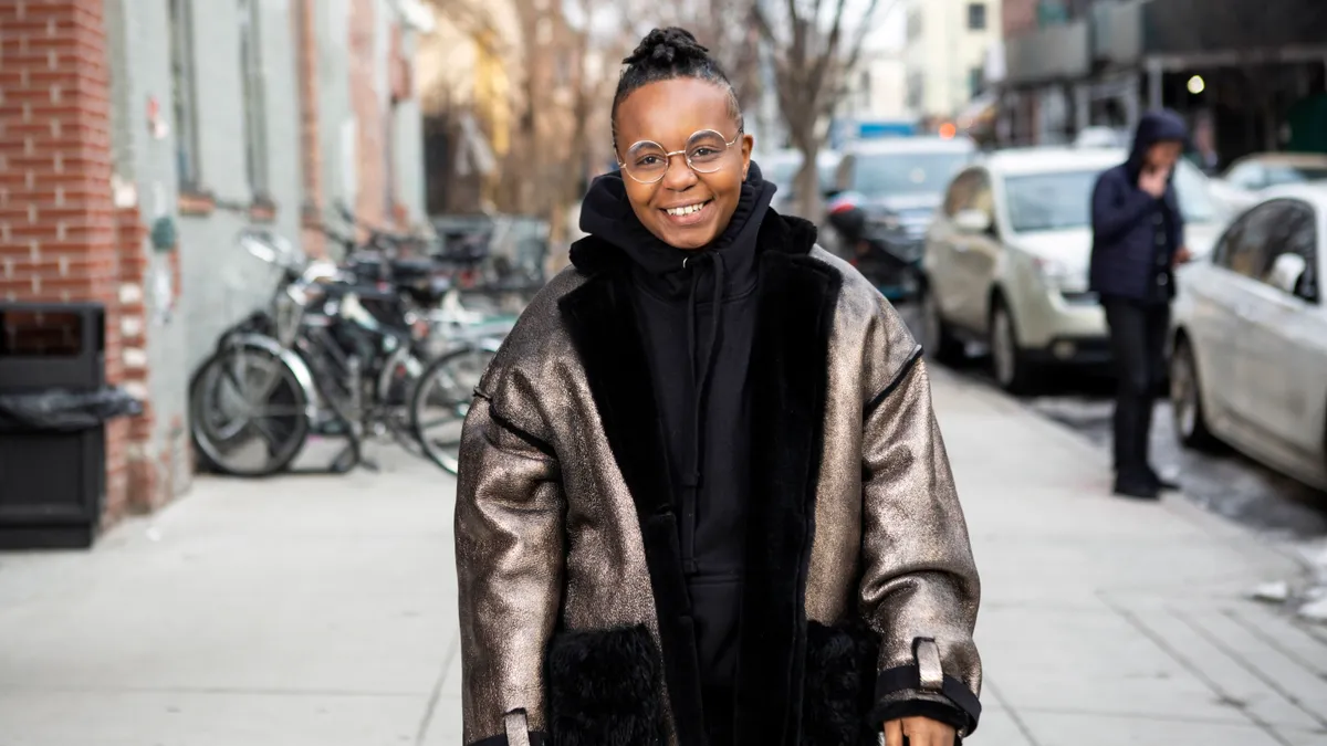 A Black transmaculine person walks down a sidewalk