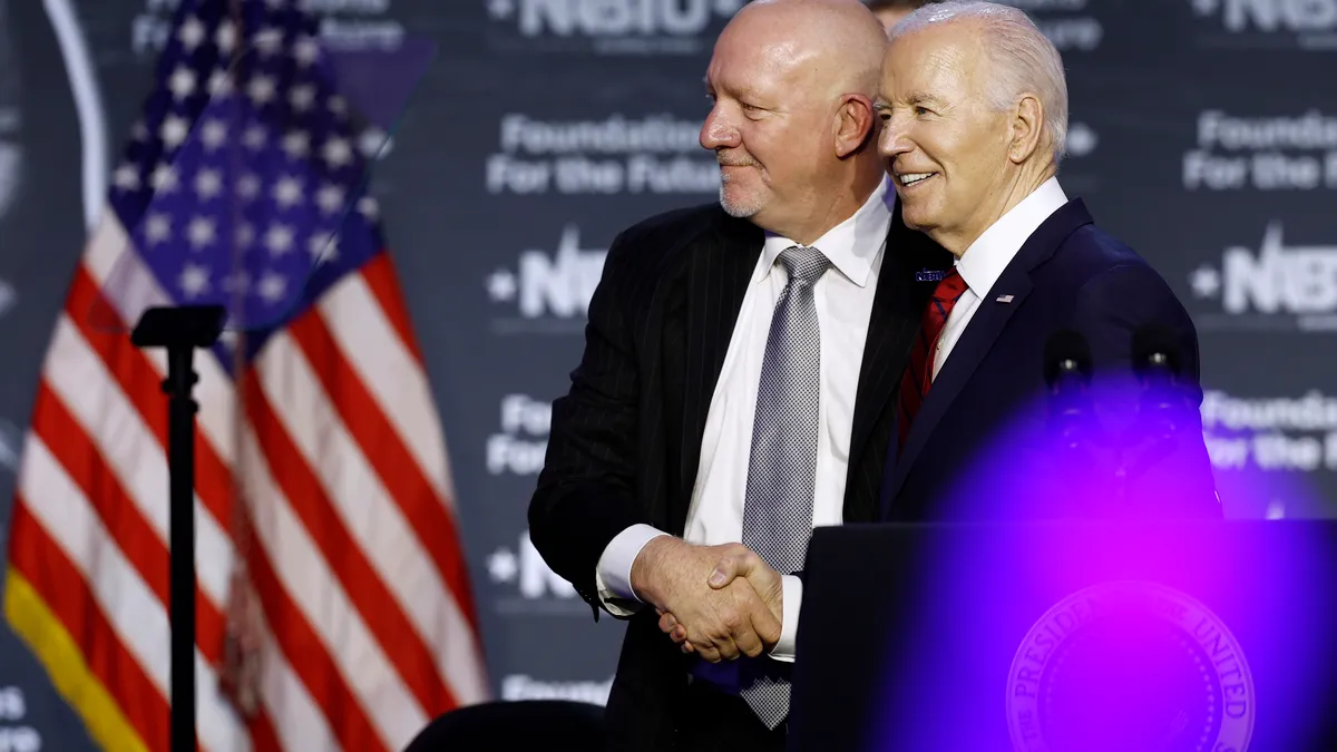 Two men shake hands on stage, posing for photographs.