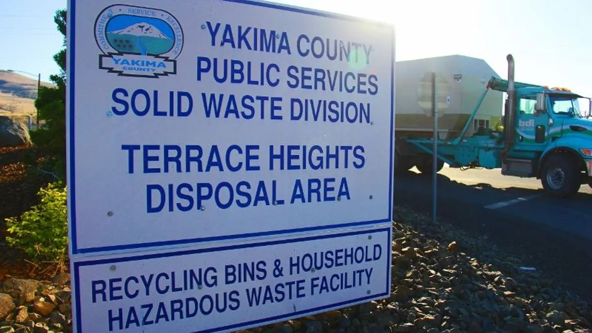 Sign reading "Yakima County Public Services Solid Waste Division - Terrace Heights Disposal Area" in front of a heavy-duty truck at an outdoor area.