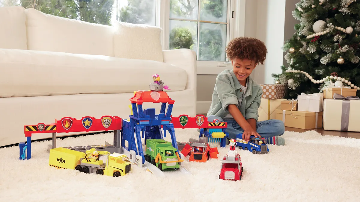 A child plays with toys on a rug next to a couch with a Christmas tree in the background.