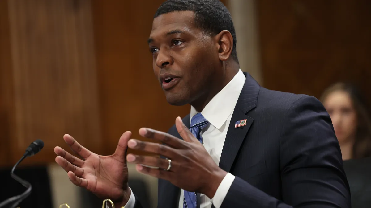 U.S. Environmental Protection Agency Administrator Michael Regan in a suit and tie speaking with a microphone in front of him and a brown background.