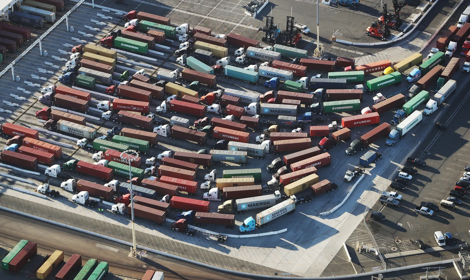 Several trucks carrying shipping containers wait in line at the Port of Los Angeles.