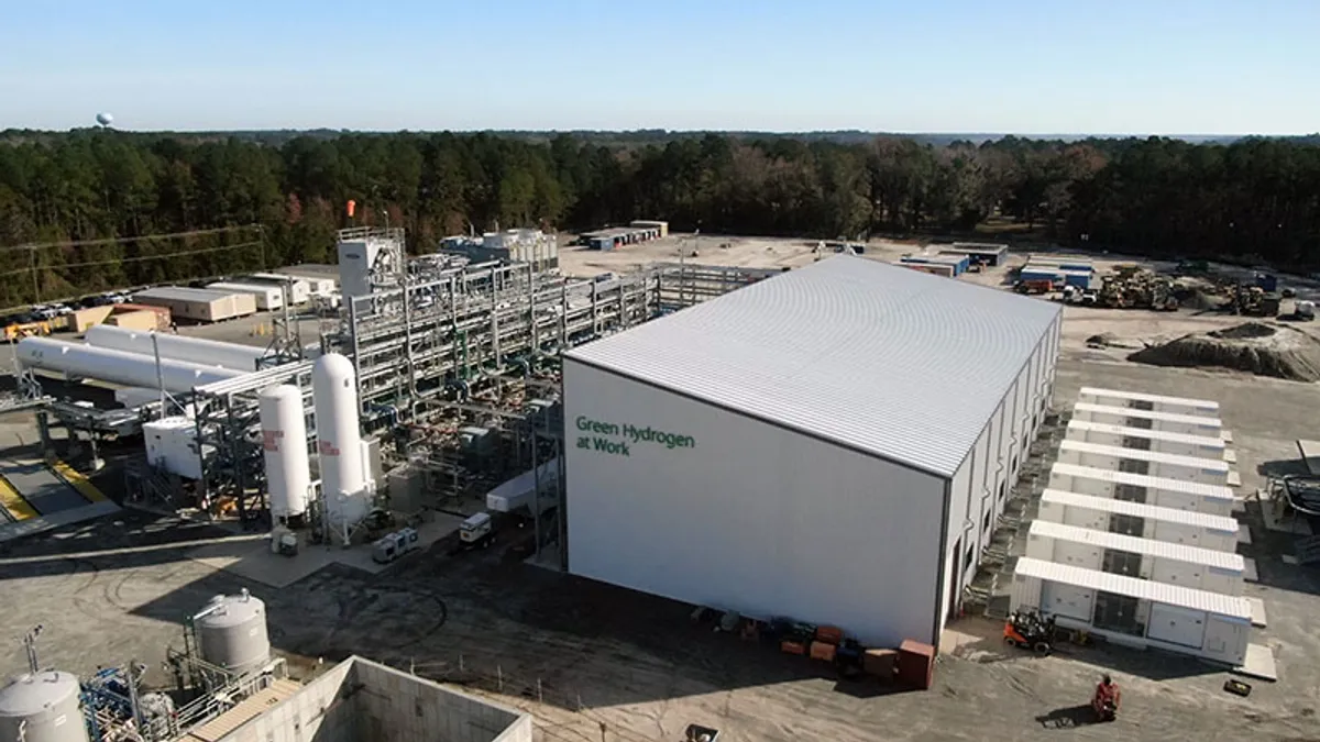 An industrial facility surrounded by trees, with the words "Green Hydrogen at Work" on the side of a large white building.