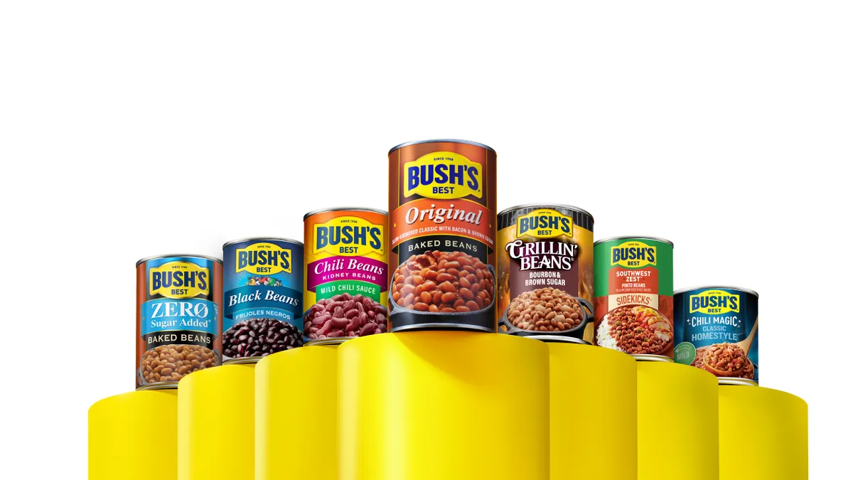 Seven cans of Bush's Best canned beans lined up next to each other (Zero-Sugar Added Baked Beans, Black Beans, Chili Beans Kidney Beans, Original Baked Beans, Grillin' Beans, Southwest Zest Pinto Beans, Chili Magic Classic Homestyle)