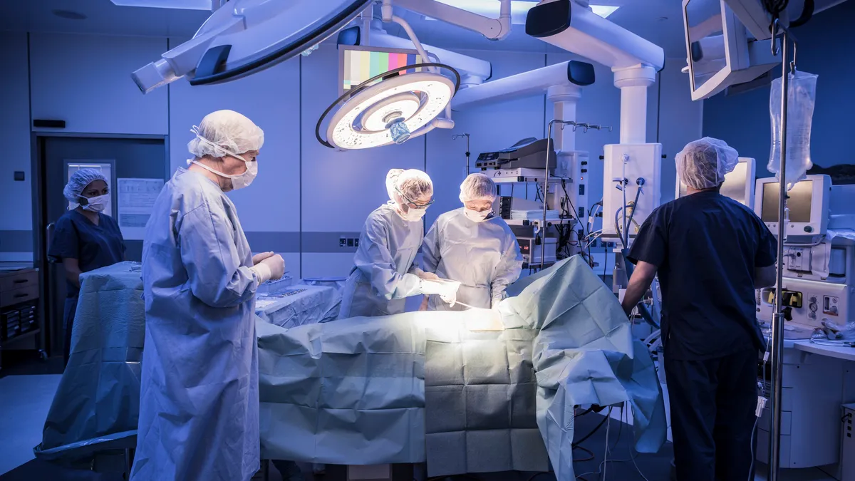 Team of surgeons operating on patient in hospital - stock photo Four doctors in hospital operating room with patient lying on operating table. Surgical lights shining on medical team performing operat