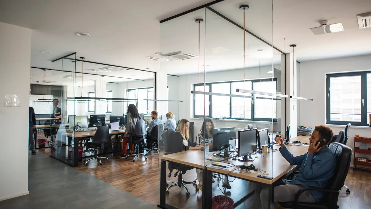 Business colleagues interact at communal workstations in a see-through open-plan office space.