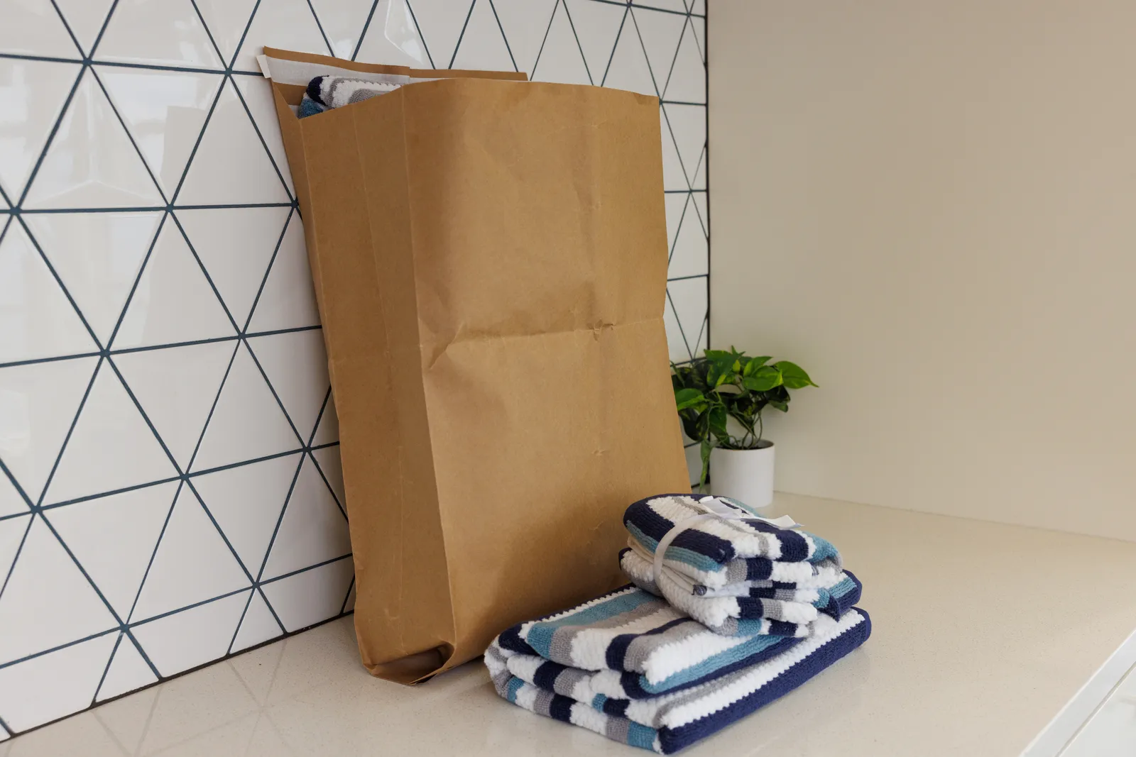 A brown paper mailer envelope with gussets at the bottom holds towels, with multicolored towels stacked next to it.