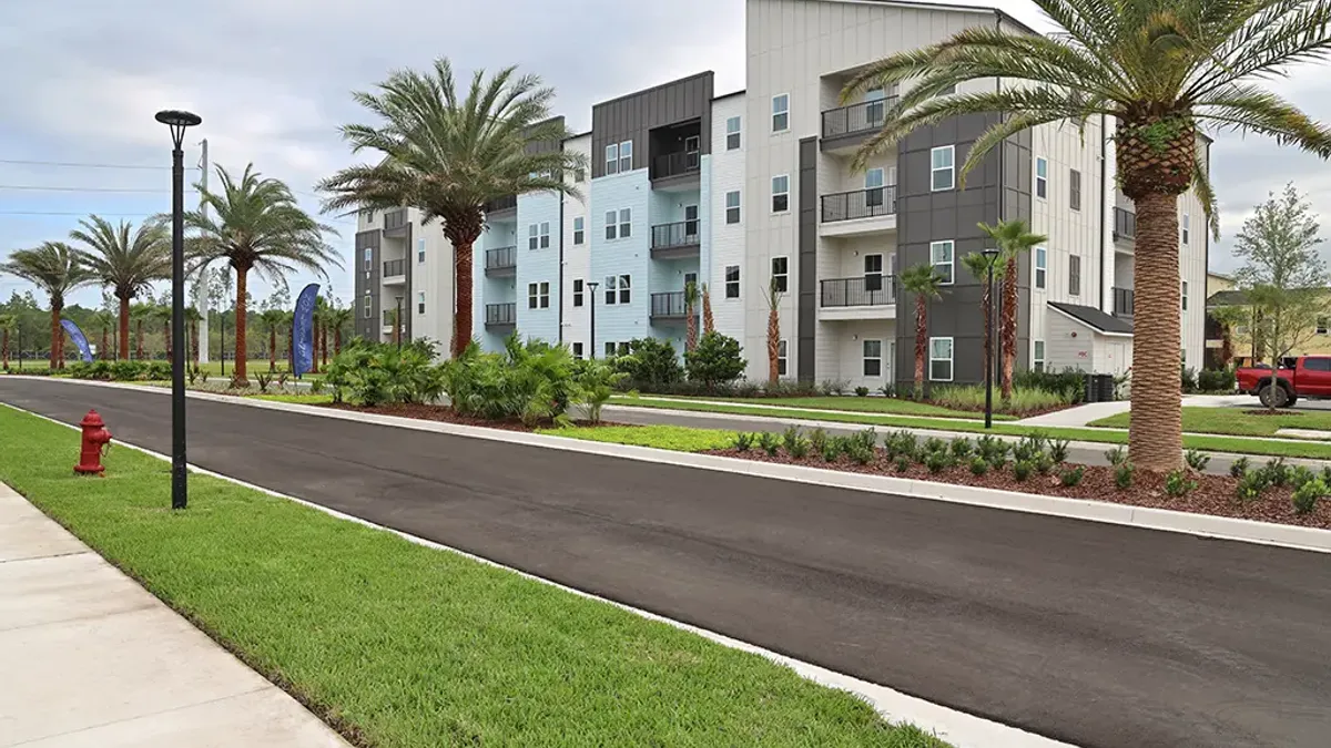 White apartments with palm trees and a road in the foreground.