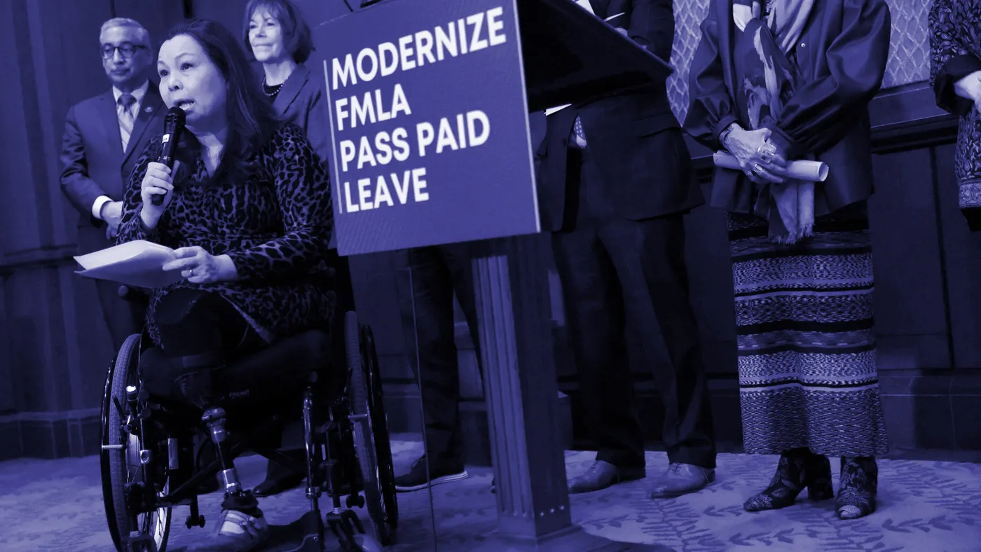 A person in a wheelchair speaks while several people stand behind them.