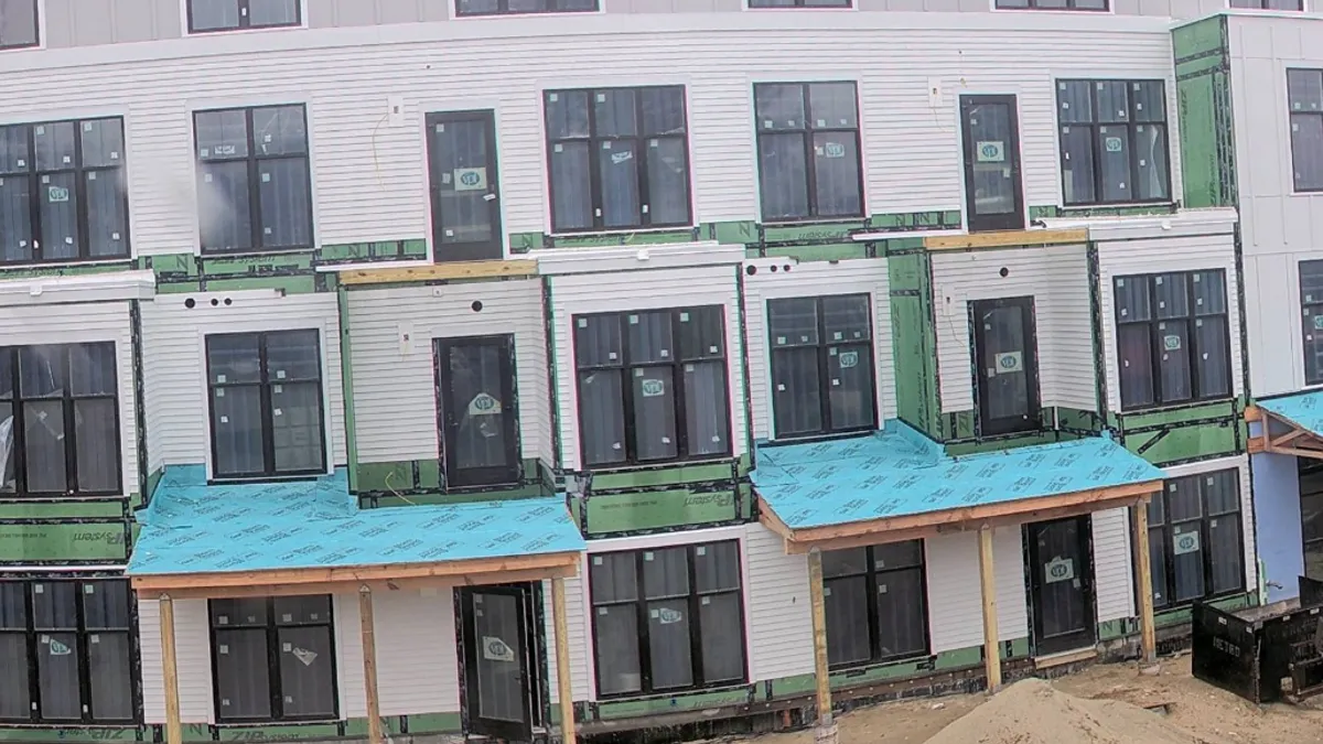 A building with white tags on all of its windows. A piece of construction equipment is parked nearby.