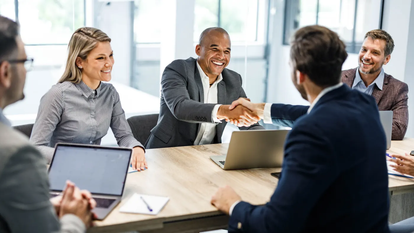 Two business people shake hands during a meeting.