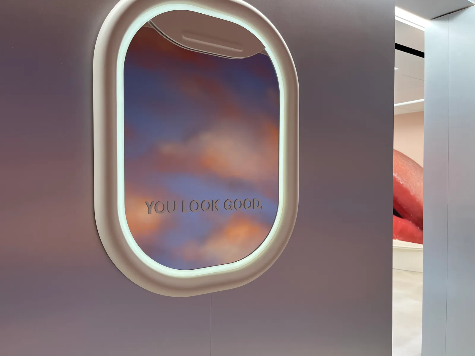 An airplane window with a mirror inside Glossier's Washington, D.C. store that says "You look good."