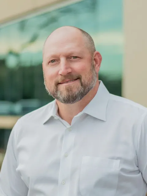 Man in a button up shirt smiles at the camera.