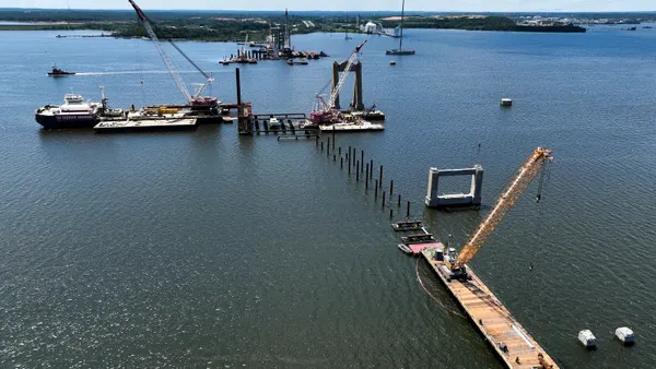 Cranes and barges near a dock as crews work in the water to construct a bridge.