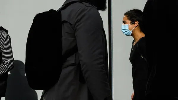 A woman wearing a protective facemask walks in the street, against other pedestrians' silhouettes