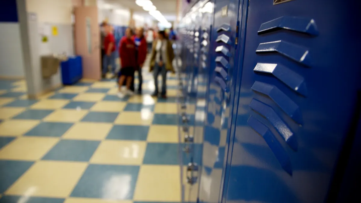 Blue school hallway lockers and checkered tile in high school with students in the background.