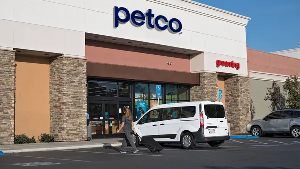 A Petco storefront. There is a white van parked outside and a person walking in the store.