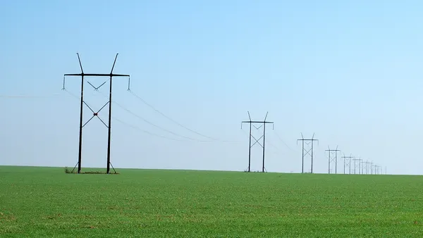 Electric power lines crossing a green field.