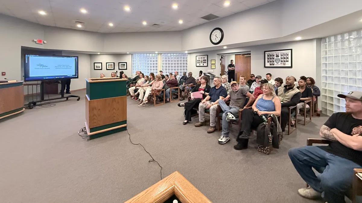 Many people seated in a large room with a podium and large TV screen.