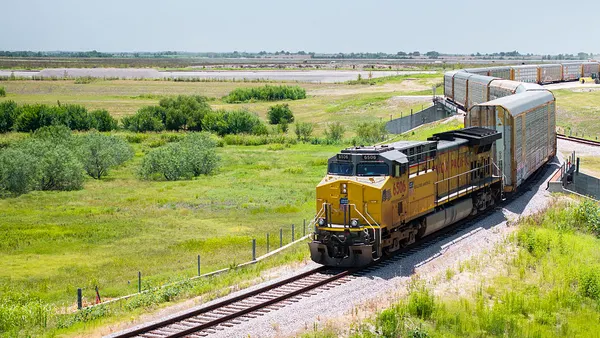 A freight train travels through a grassy green landscape on a sunny day.
