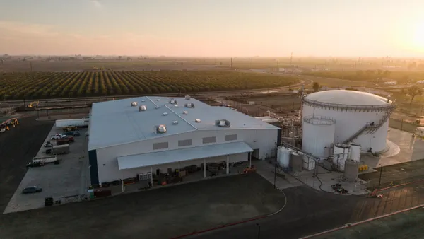 Aerial view of a large industrial shed taken with the sun low in the horizon. Agricultural fields are visible in the background.