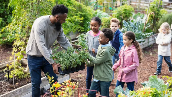 A handful of children are in a garden. An adult is showing the children some plants.