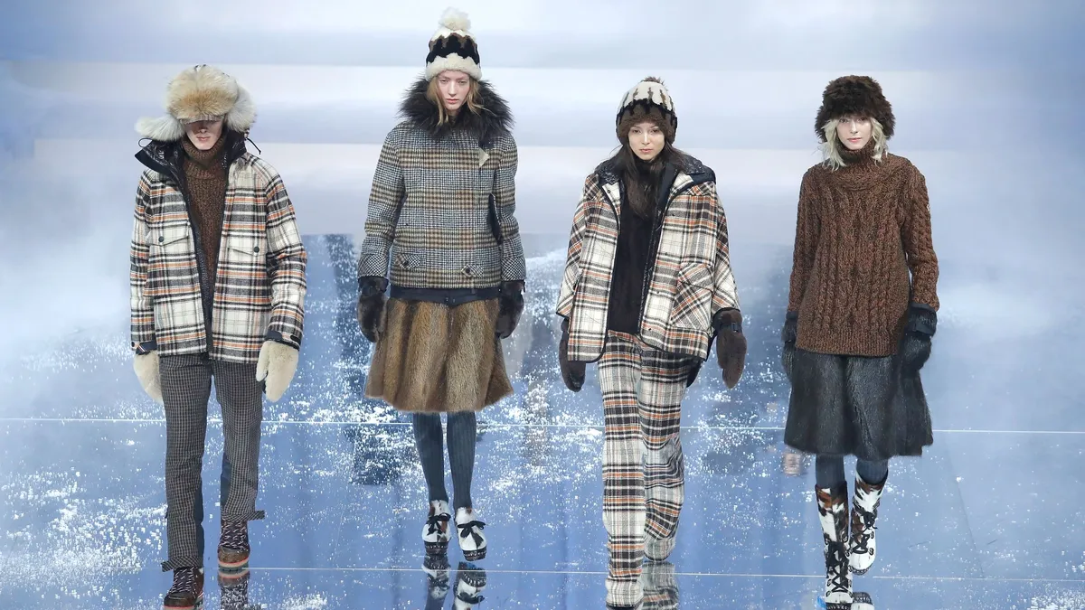 Models in plaid outerwear walk on a glass runway.