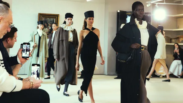 Models walk down a salon-style runway wearing muted neutral colors and coats.