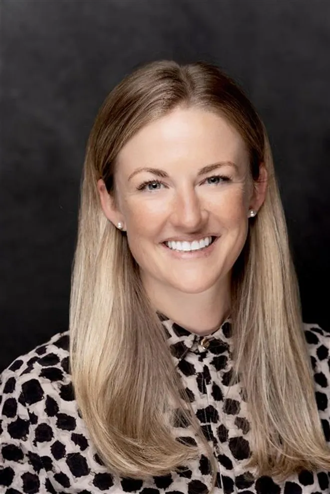 Headshot of a white, blonde woman in a leopard button up, charcoal background