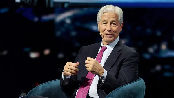JPMorgan Chase CEO Jamie Dimon sits in a blue velvet chair on a stage with a dark background behind him.
