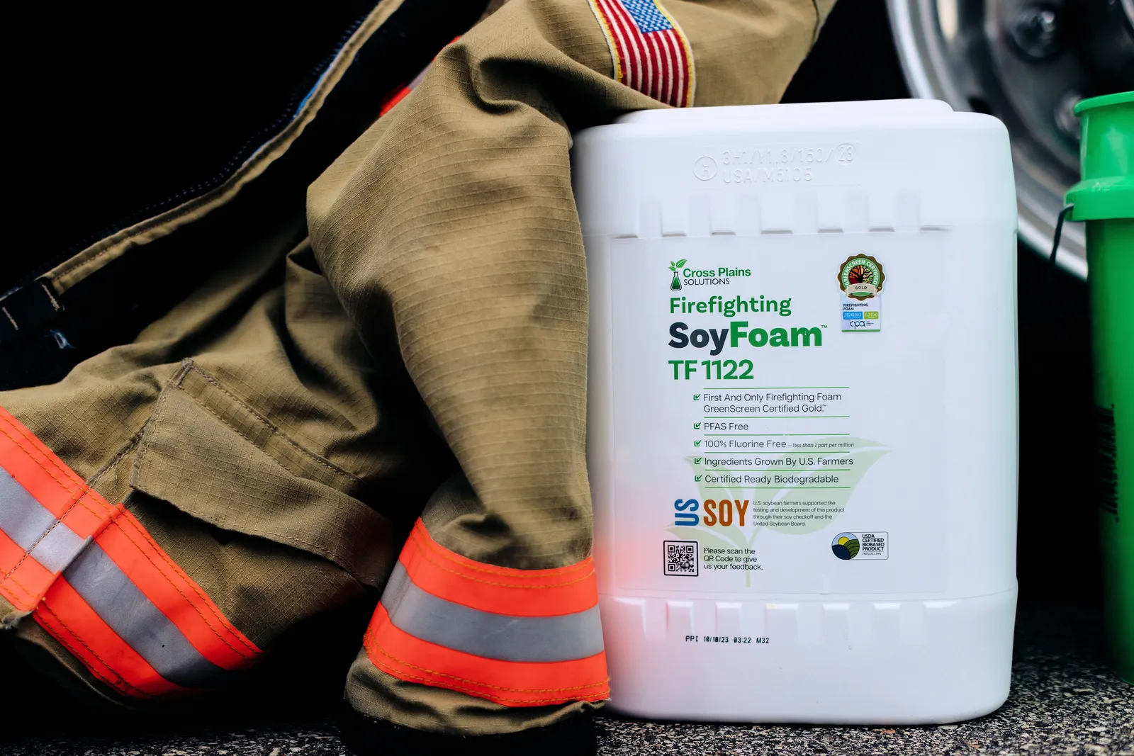 A white container with Cross Plains Solutions green logo, set next to a yellow and orange firefighter coat.