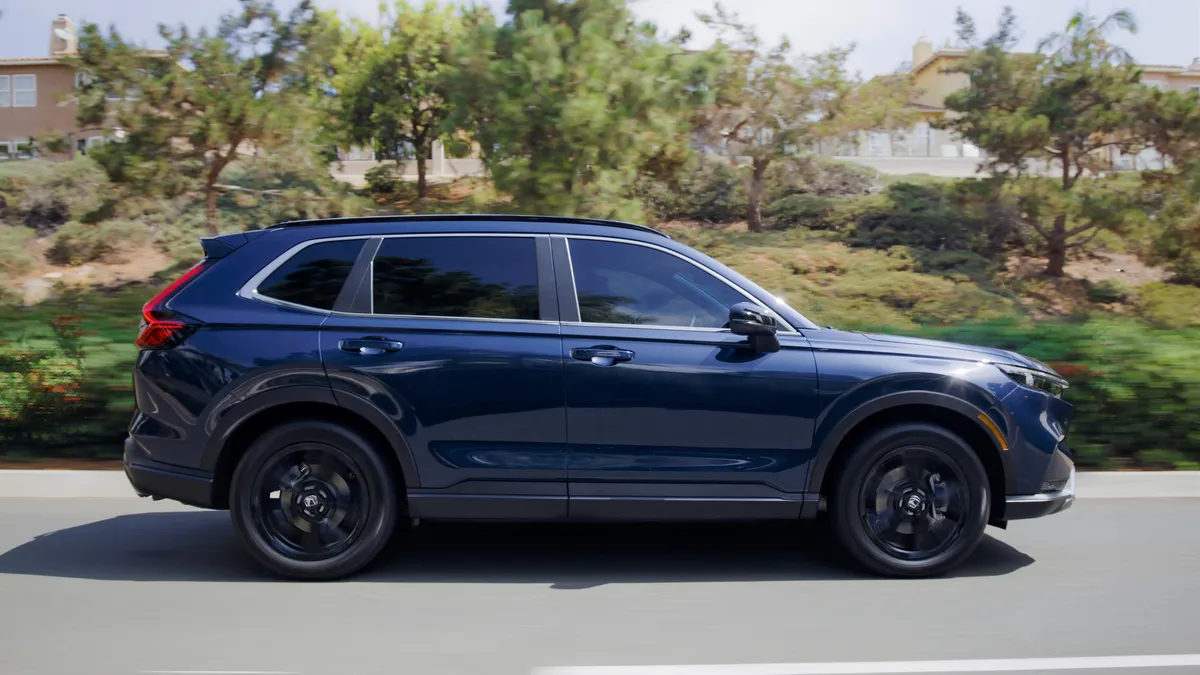 A 2023 Honda CR-V hybrid crossover on a highway with trees and homes in the background.