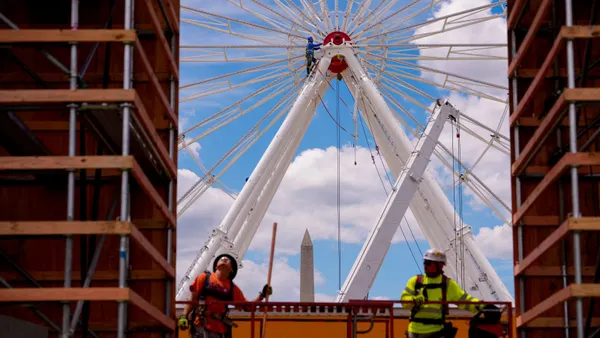 Two construction workers below a Ferris wheel with the Washington Monument in the background.