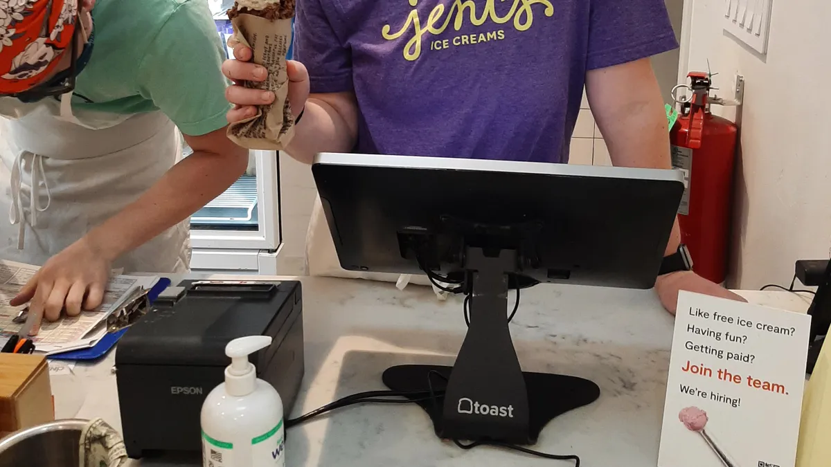 Woman standing behind counter and cash register serves ice cream cone.