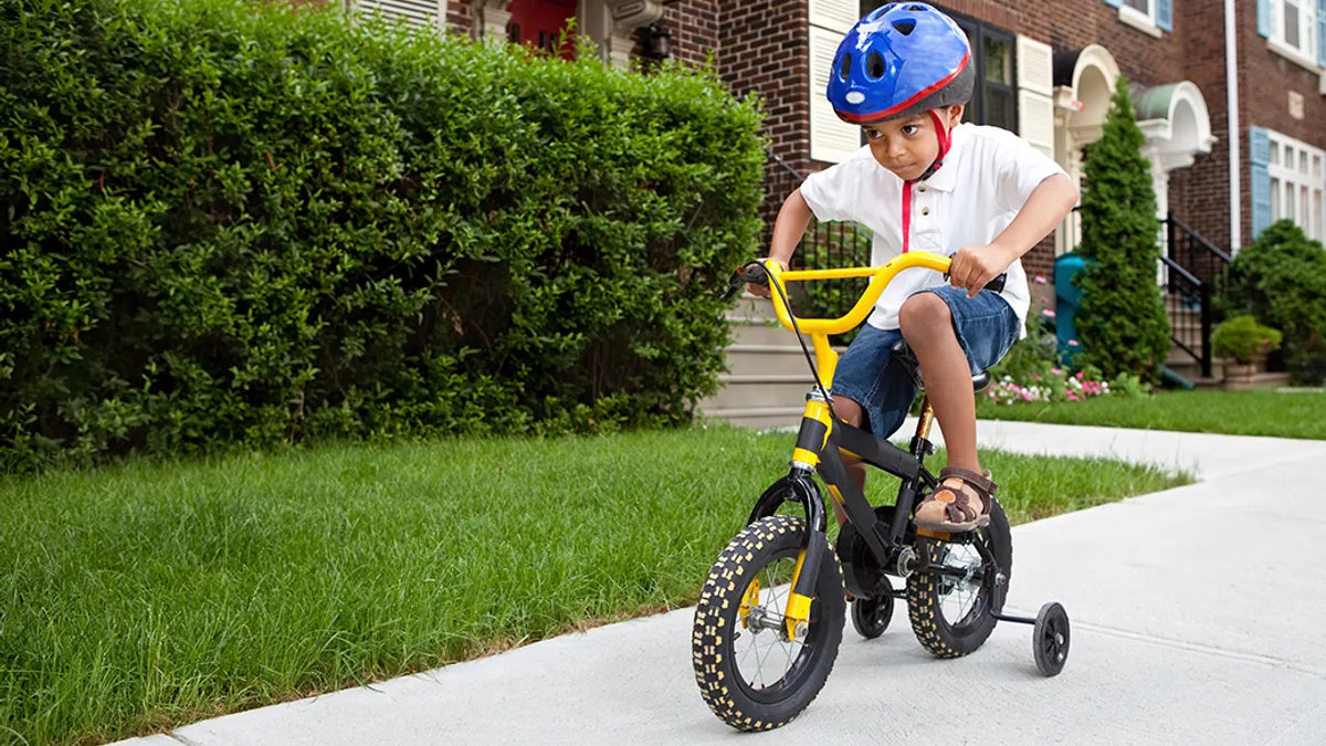 Young boy riding his first bicycle with training wheels