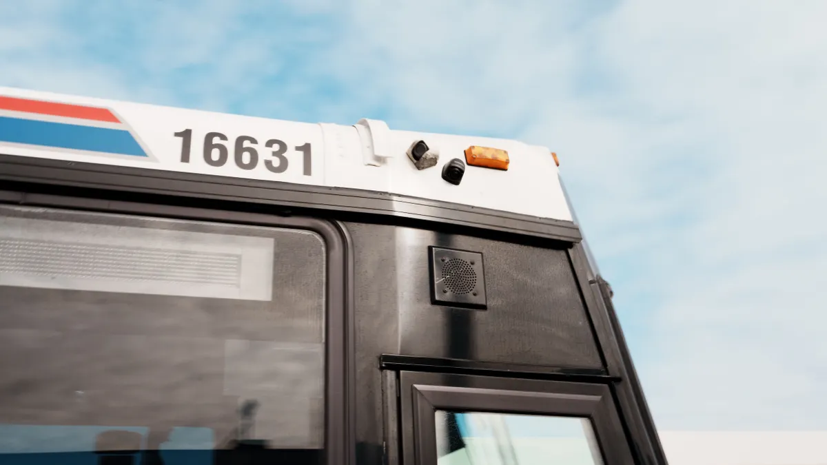 View looking up toward the right-side front of a large bus, with two small cameras mounted above the front door.
