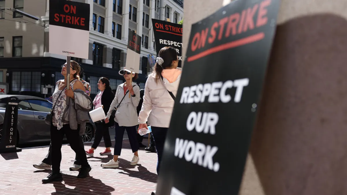 A sign reading "Respect our work" is in the foreground. Workers holding picket signs march in the background.