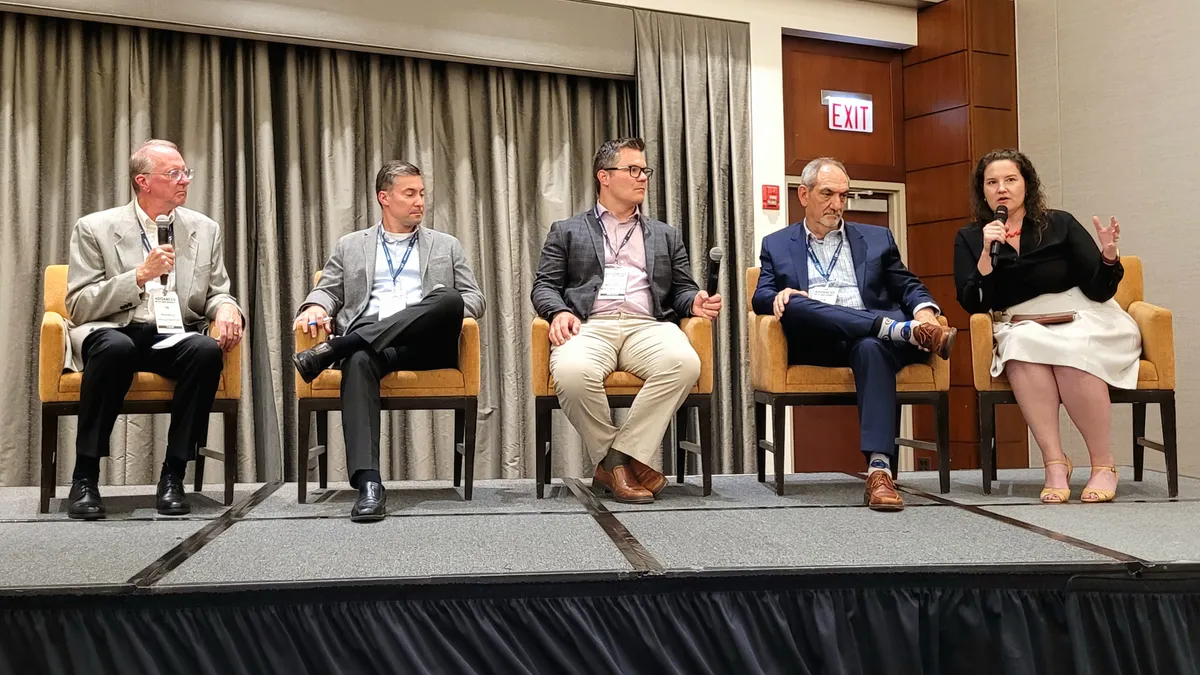 Five speakers on a stage at a conference.