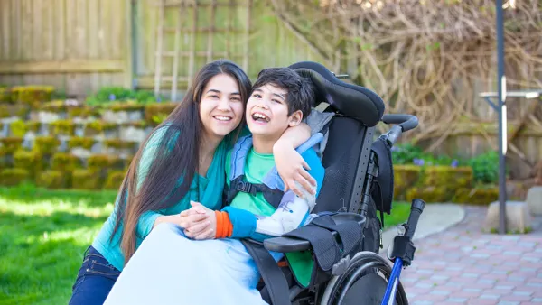 A special needs kid in a wheelchair smiling and being hugged by an adult