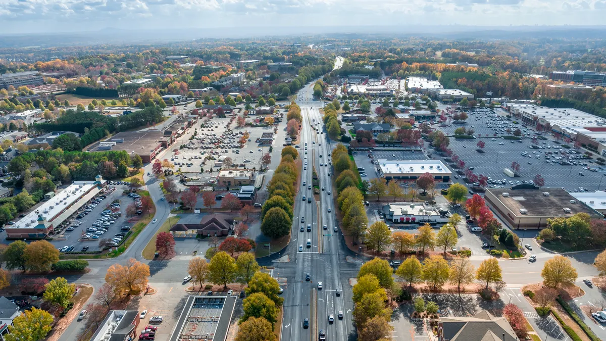 An aerial view of the Atlanta suburbs shows trees, buildings, cars in parking lots and on roads.