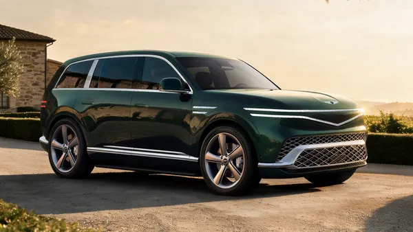 A right-side exterior view of a dark green painted Genesis GV90 electric SUV parked outdoors.
